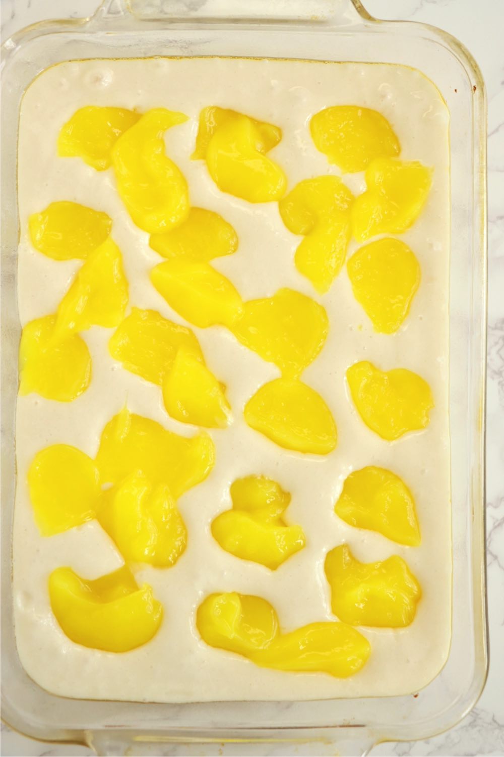 Dollops of lemon pie filling on top of cake mix in a glass baking pan.