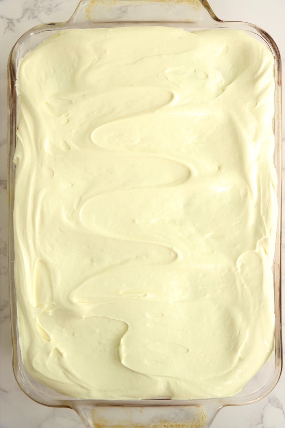 Frosting on top of lemon cake in glass baking pan.