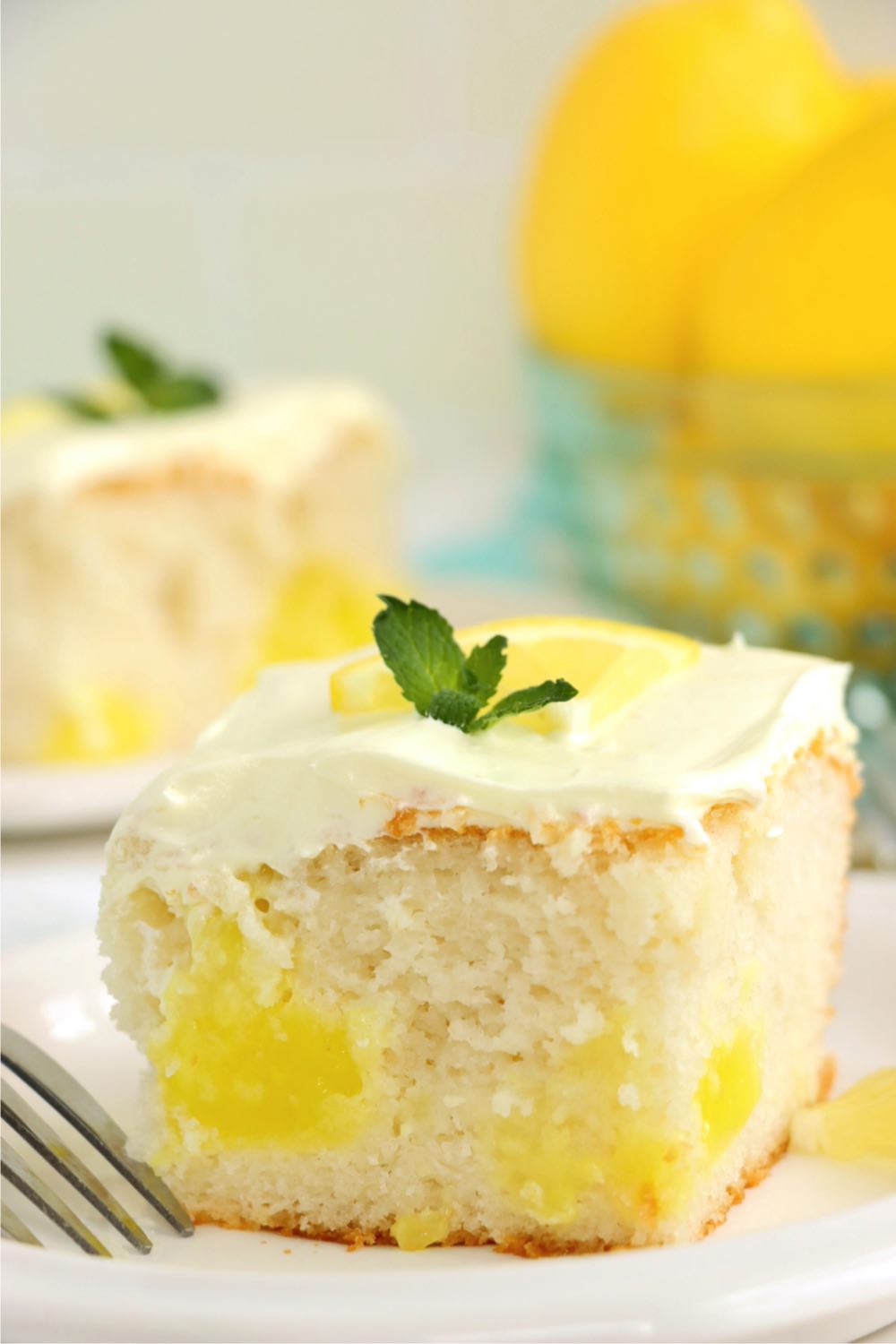 Piece of lemon cake garnished with a tiny mint leaf.