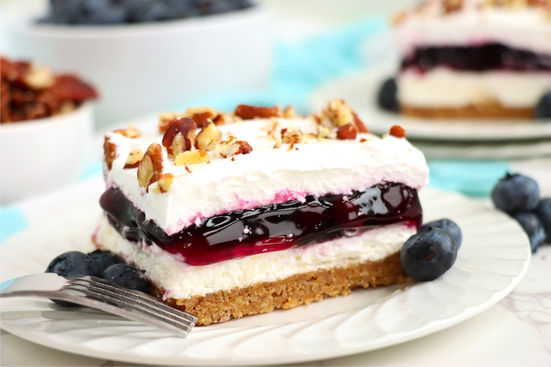 Piece of layered blueberry dessert on a white plate.