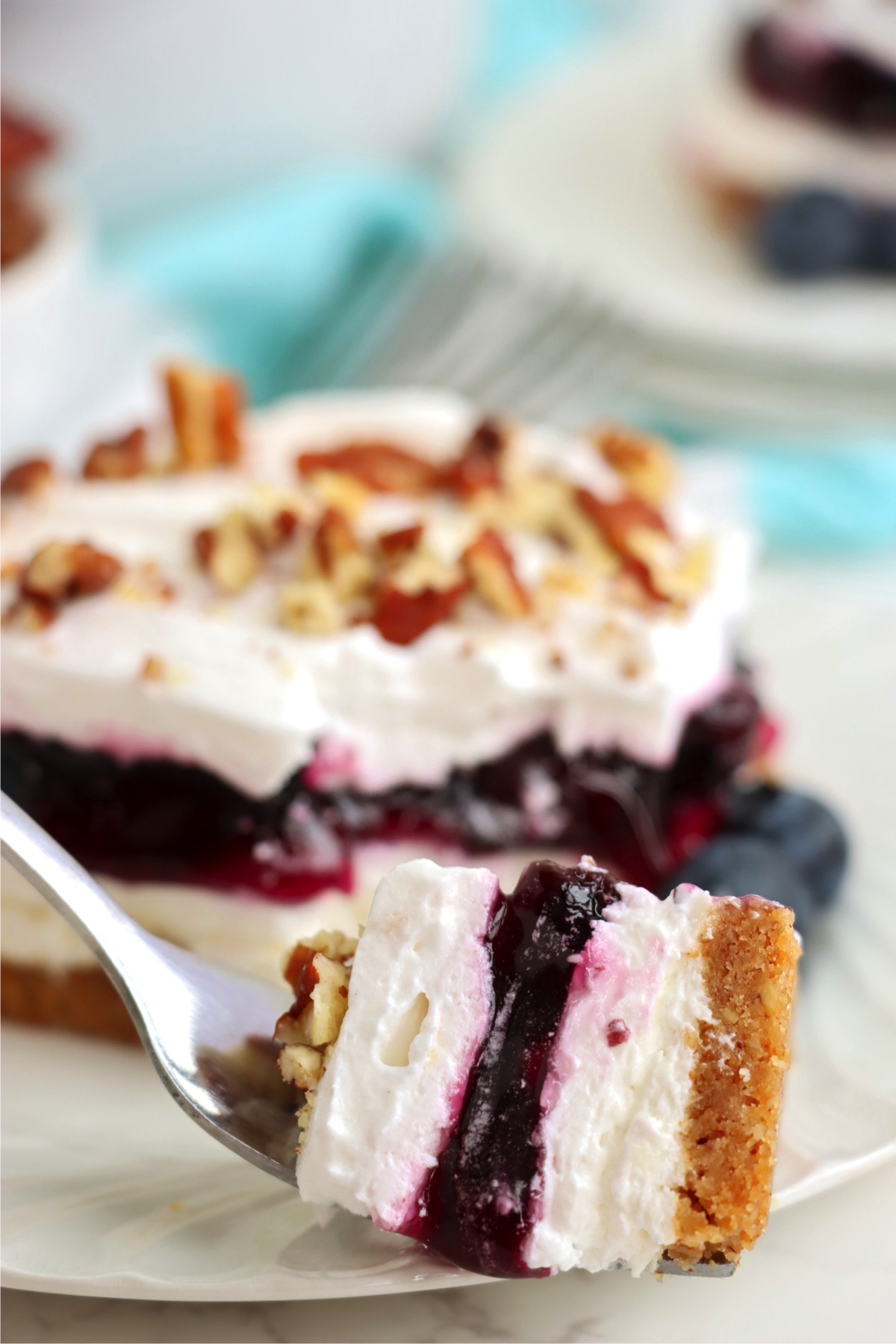 Fork holding piece of blueberry layered dessert.