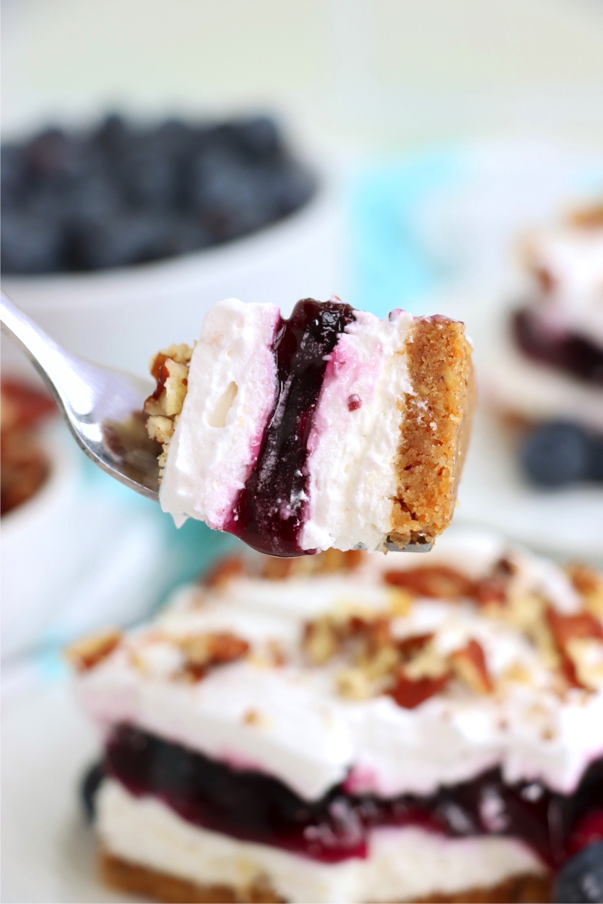 Piece of blueberry layered dessert on a fork being held up to the camera.