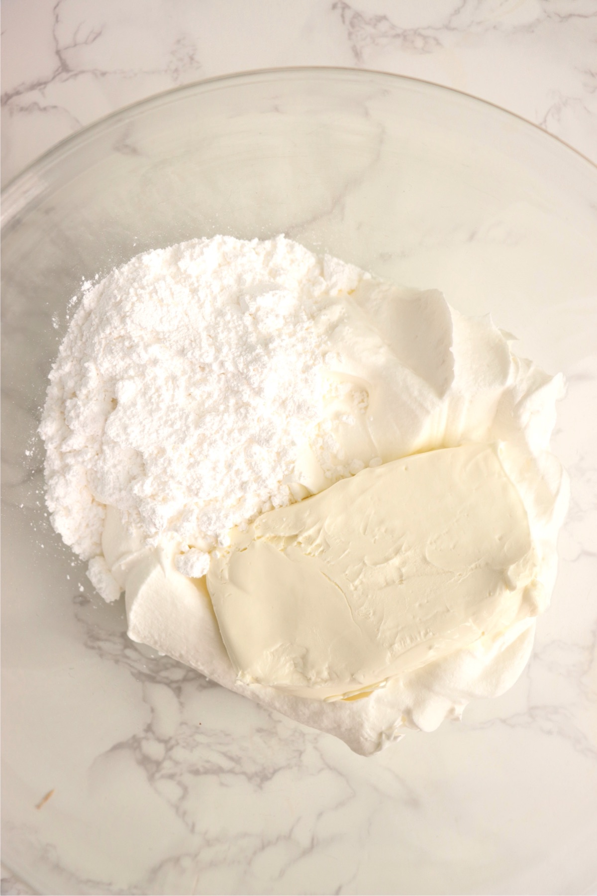 Block of cream cheese and powdered sugar in a bowl.