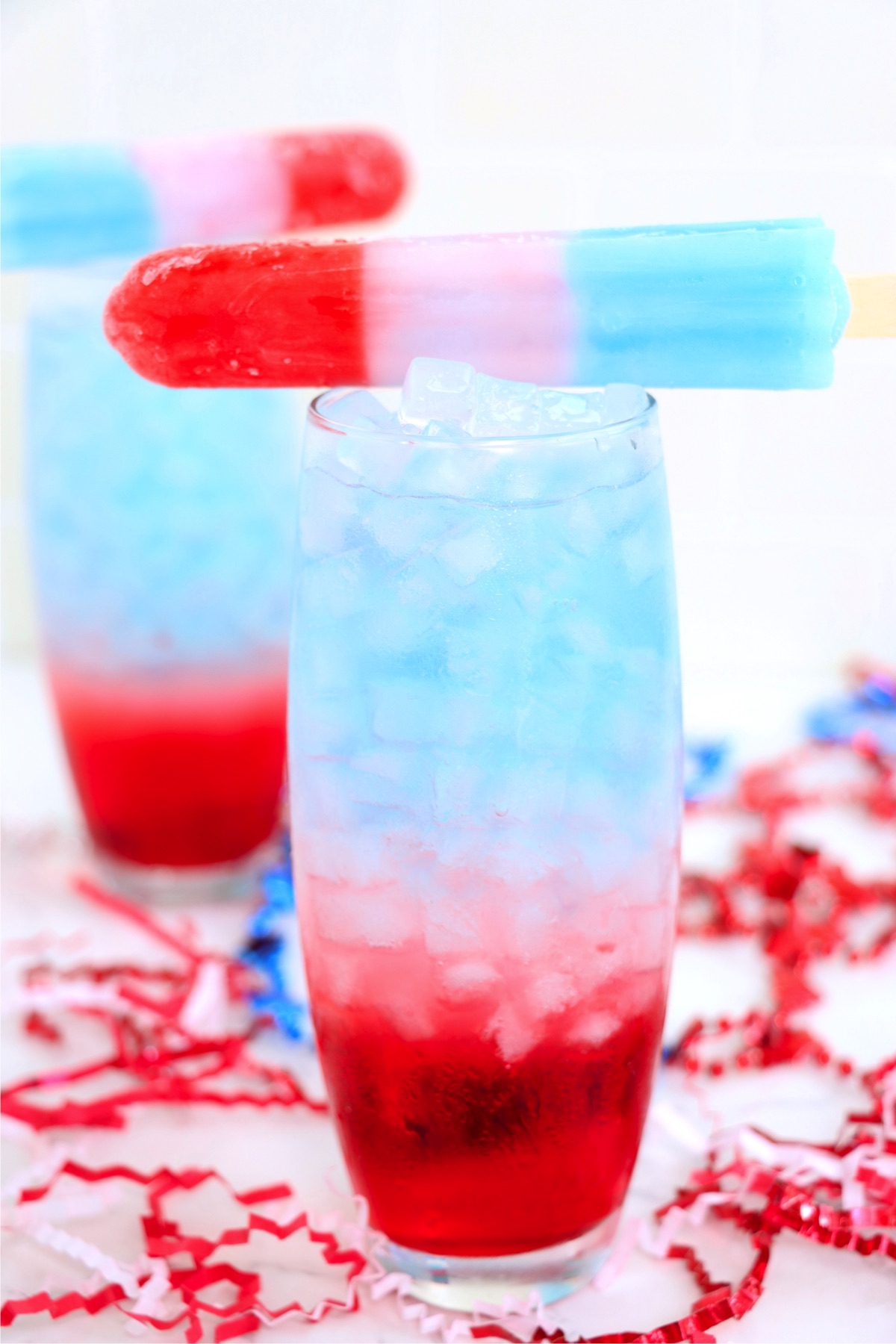 Two red, white and blue cocktails garnished with Bomb Pop popsicles.