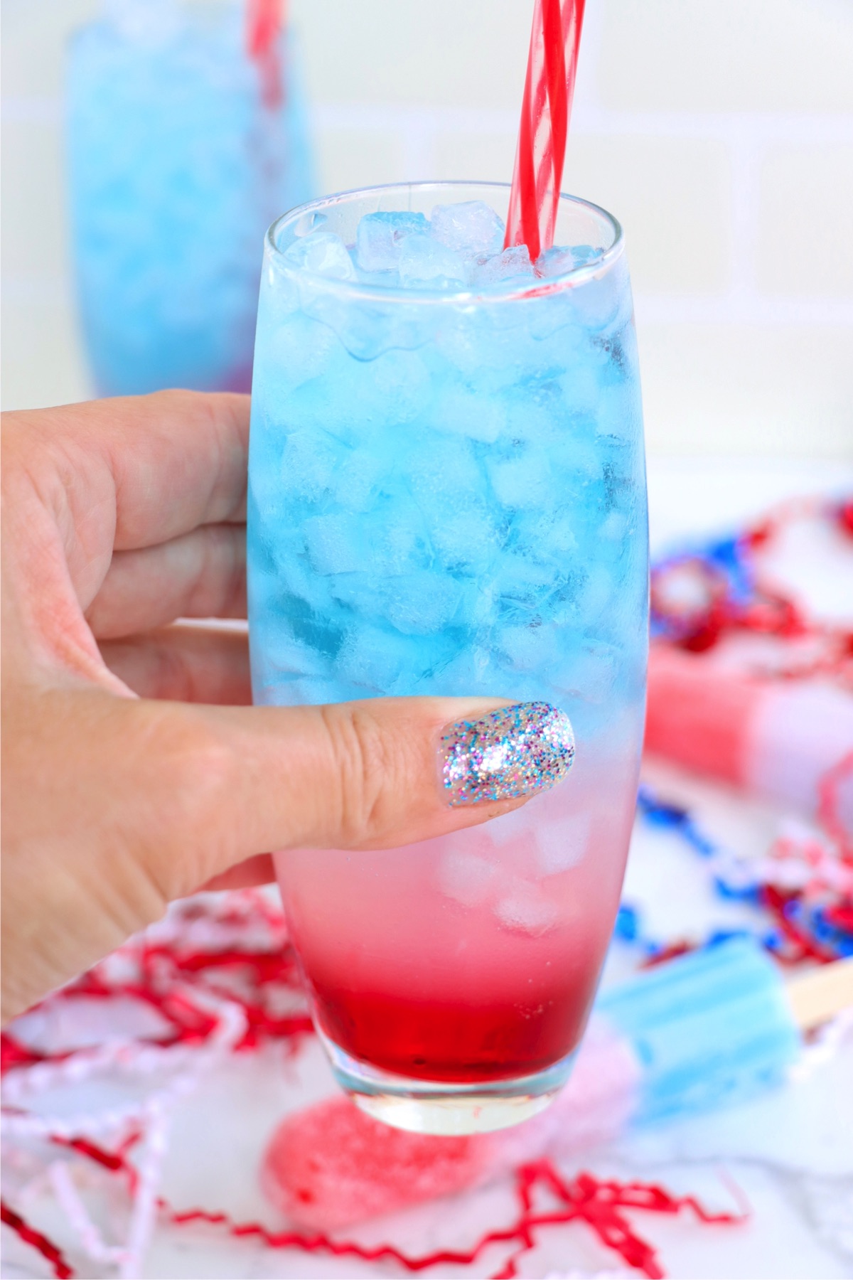 Hand holding a red, white and blue cocktail with red and white striped straw.