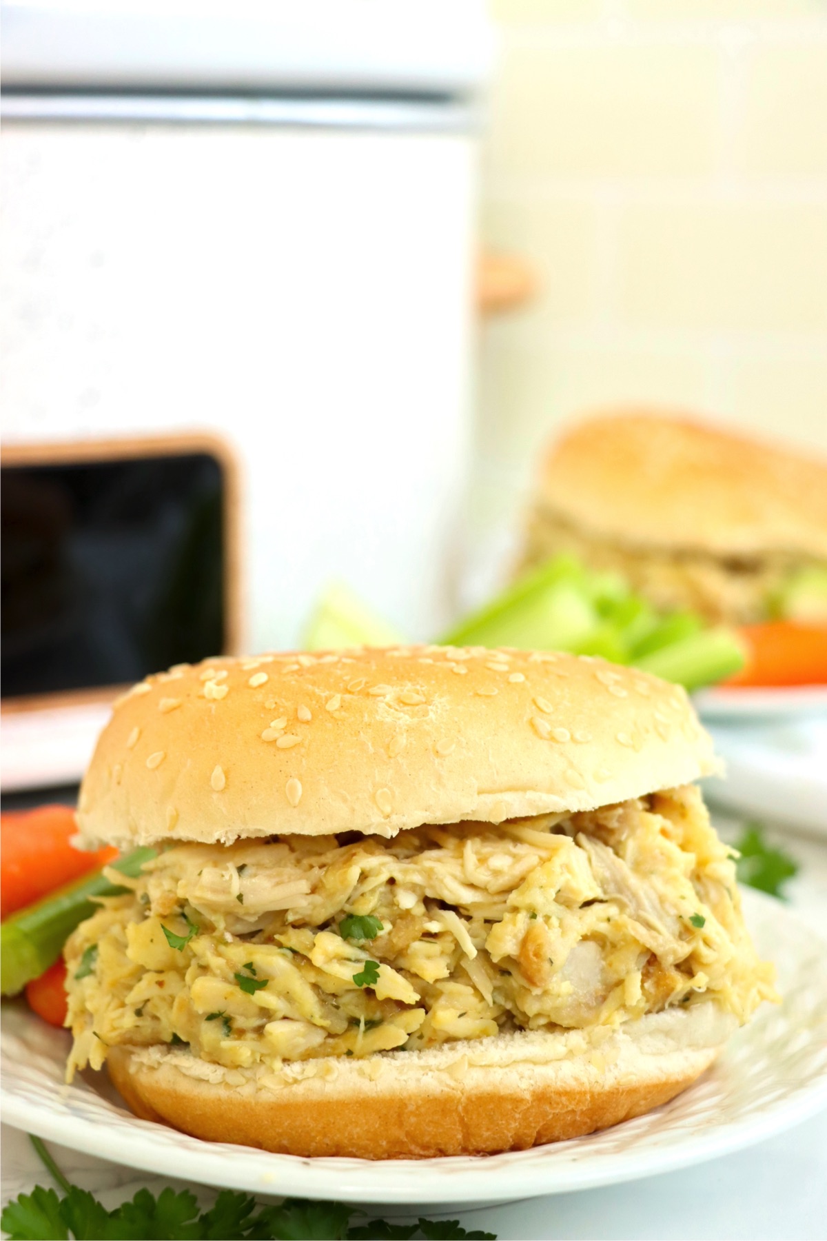 Shredded chicken on a white plate in front of a white crock pot.