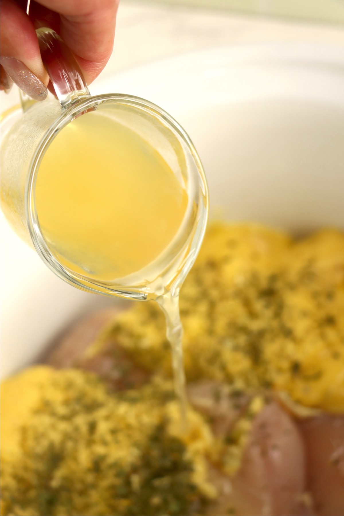 Pouring in chicken broth to crock pot with chicken breasts.