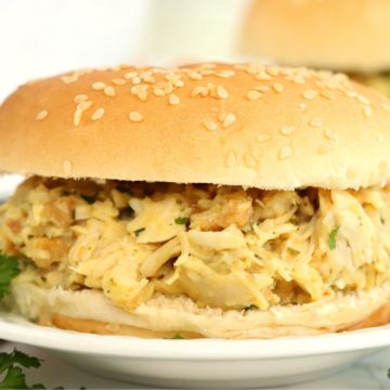 Creamy, shredded chicken sandwich on a small white plate garnished with parsley.