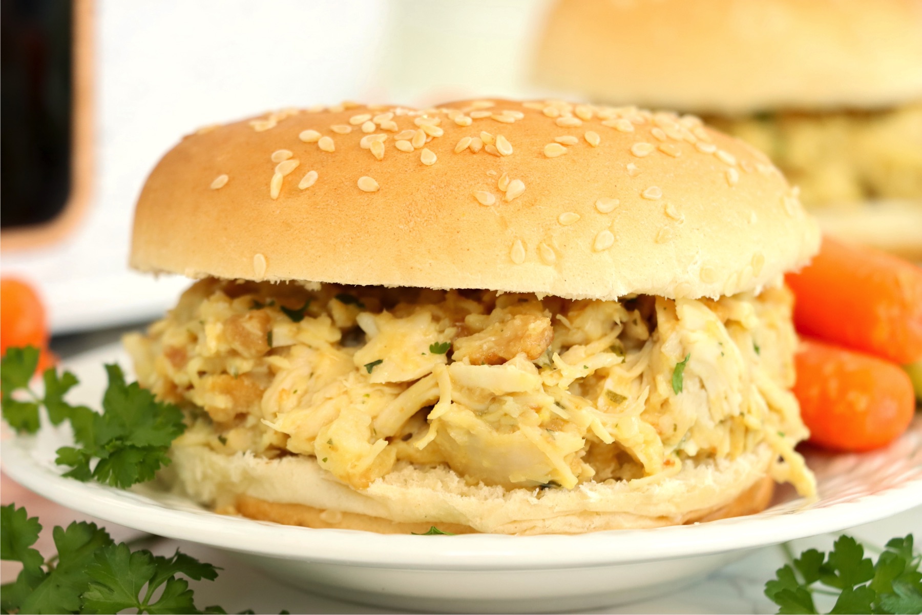 Creamy, shredded chicken sandwich on a small white plate garnished with parsley.