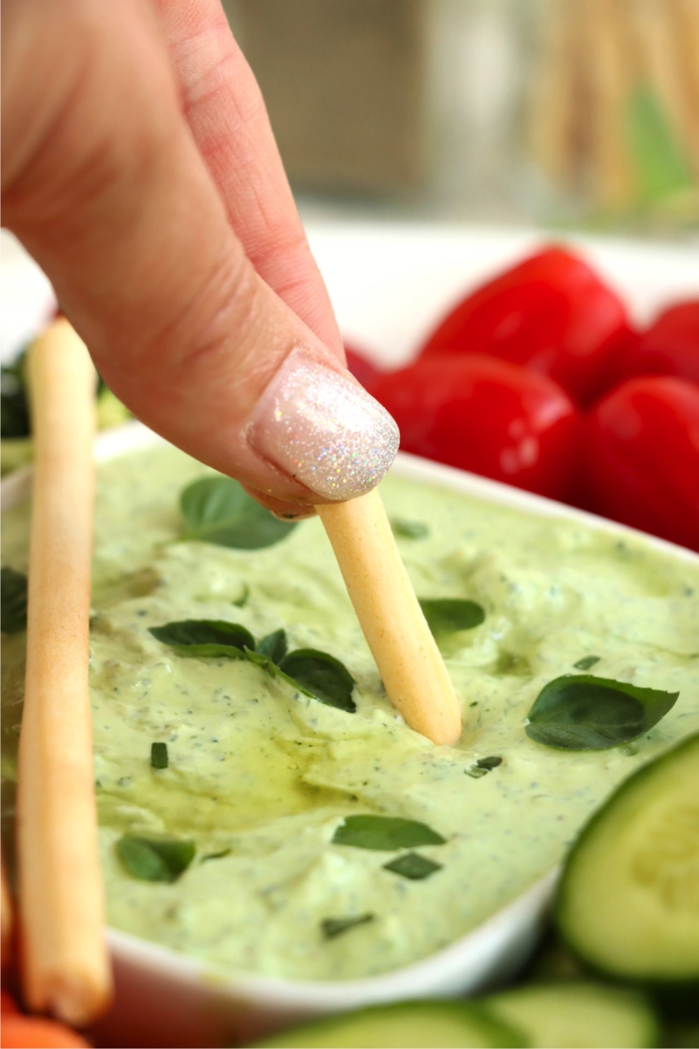 Breadstick being dipped into a green avocado dip.