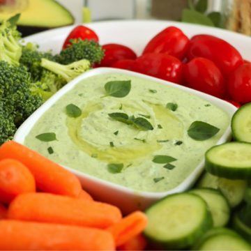 Carrots, cucumbers, tomatoes and broccoli on a platter with a bowl of green avocado dip.