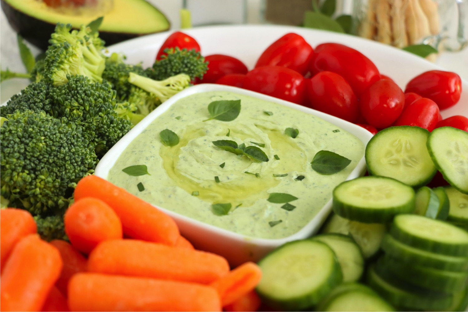 Carrots, cucumbers, tomatoes and broccoli on a platter with a bowl of green avocado dip.