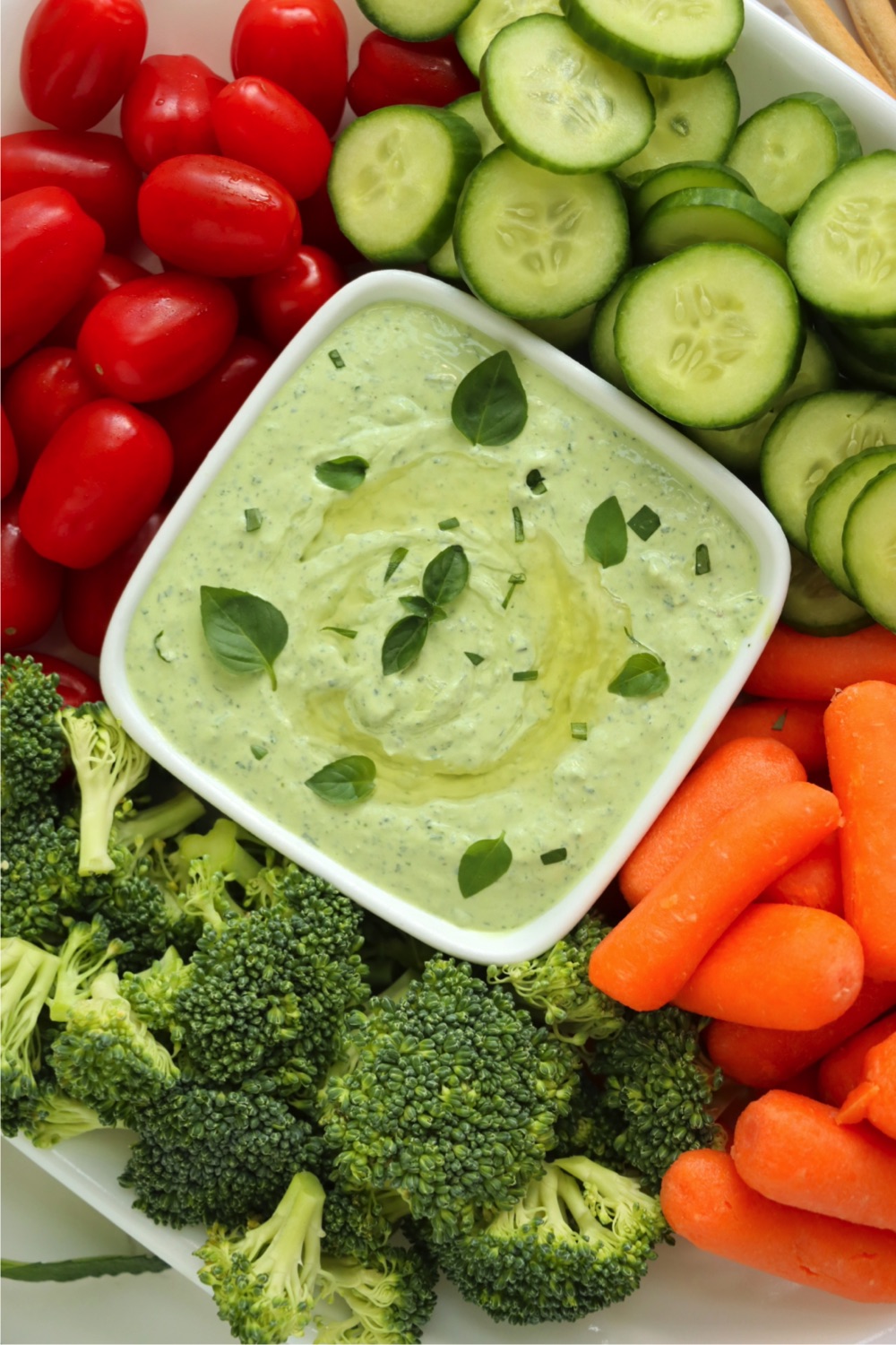 Small bowl of green dip surrounded by fresh vegetables.