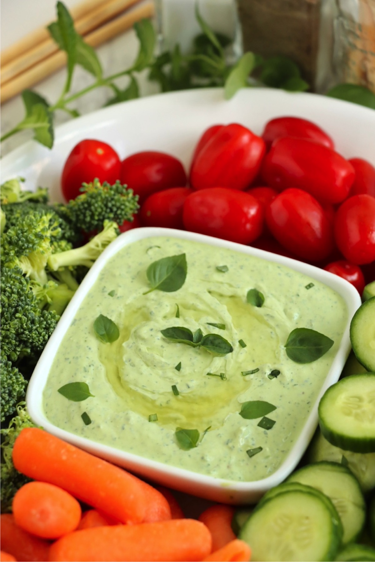 A white bowl of green dip surrounded by vegetables on a platter.