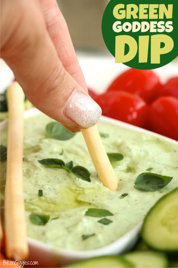 Small breadstick being dipped into avocado dip garnished with olive oil and fresh herbs.