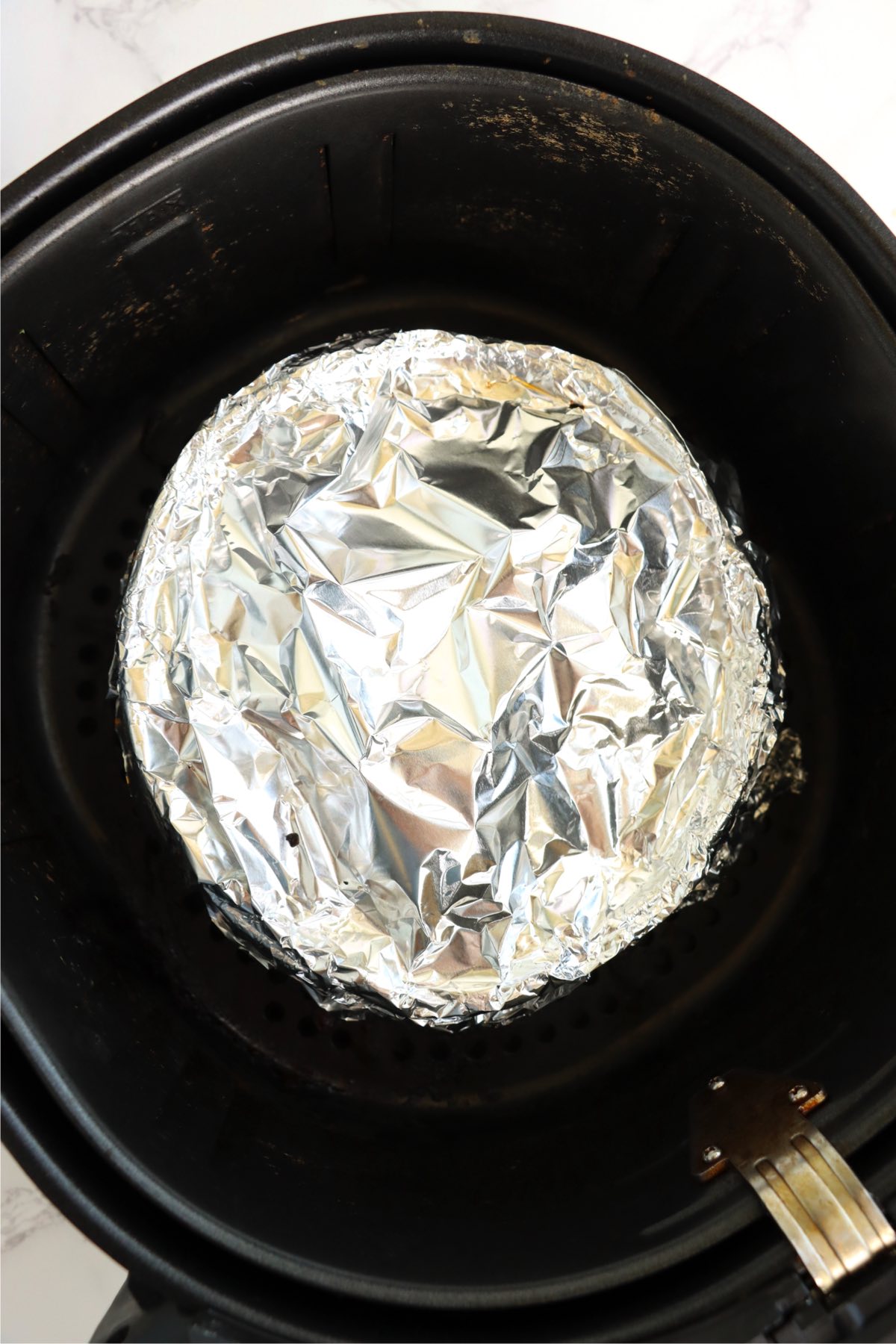 Baking pan inside of an air fryer covered with aluminum foil.