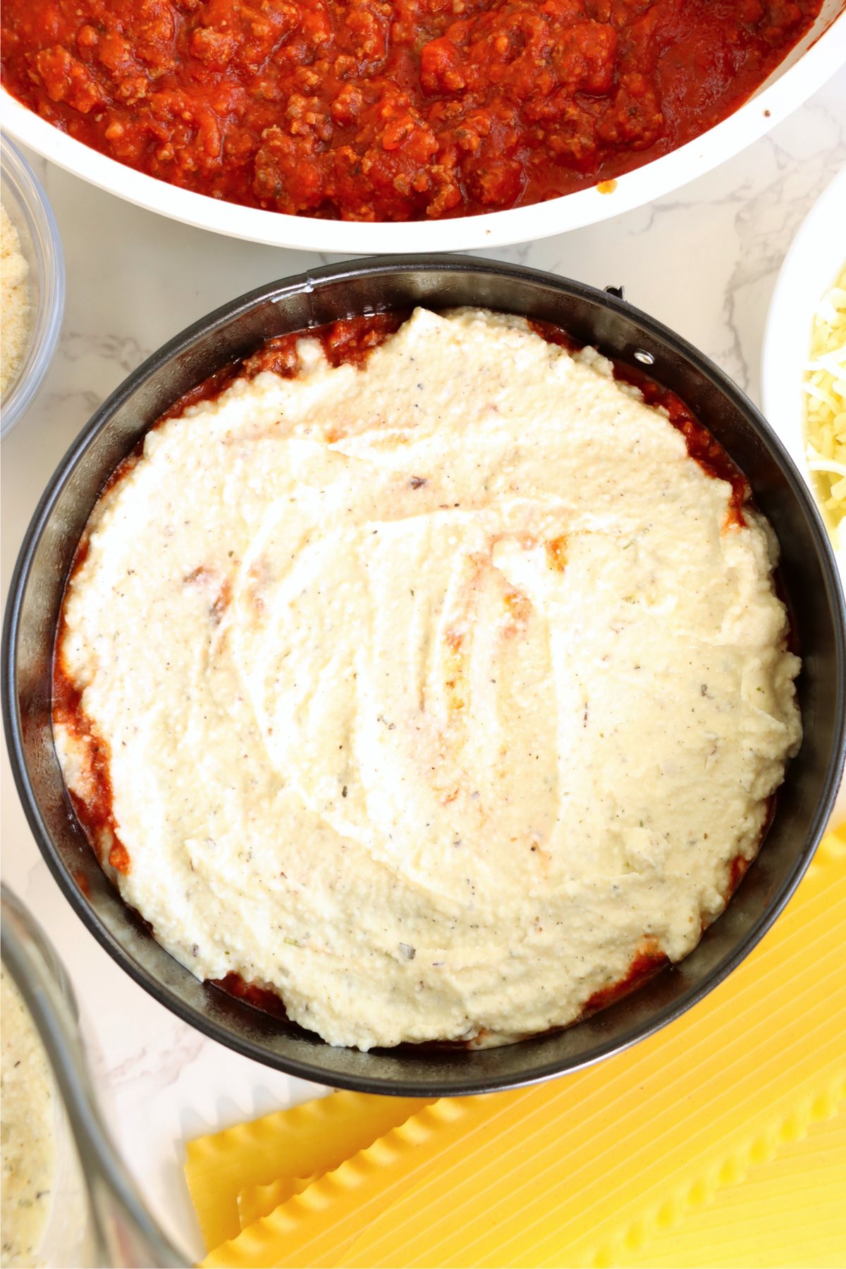 Ricotta mixture layered over meat sauce in a small round pan.