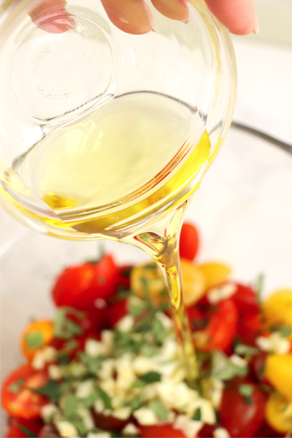 Pouring olive oil into a bowl of tomatoes and fresh herbs.