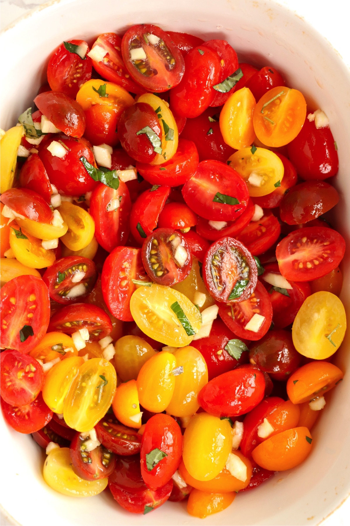 Halved cherry tomatoes in a pan mixed with fresh basil.