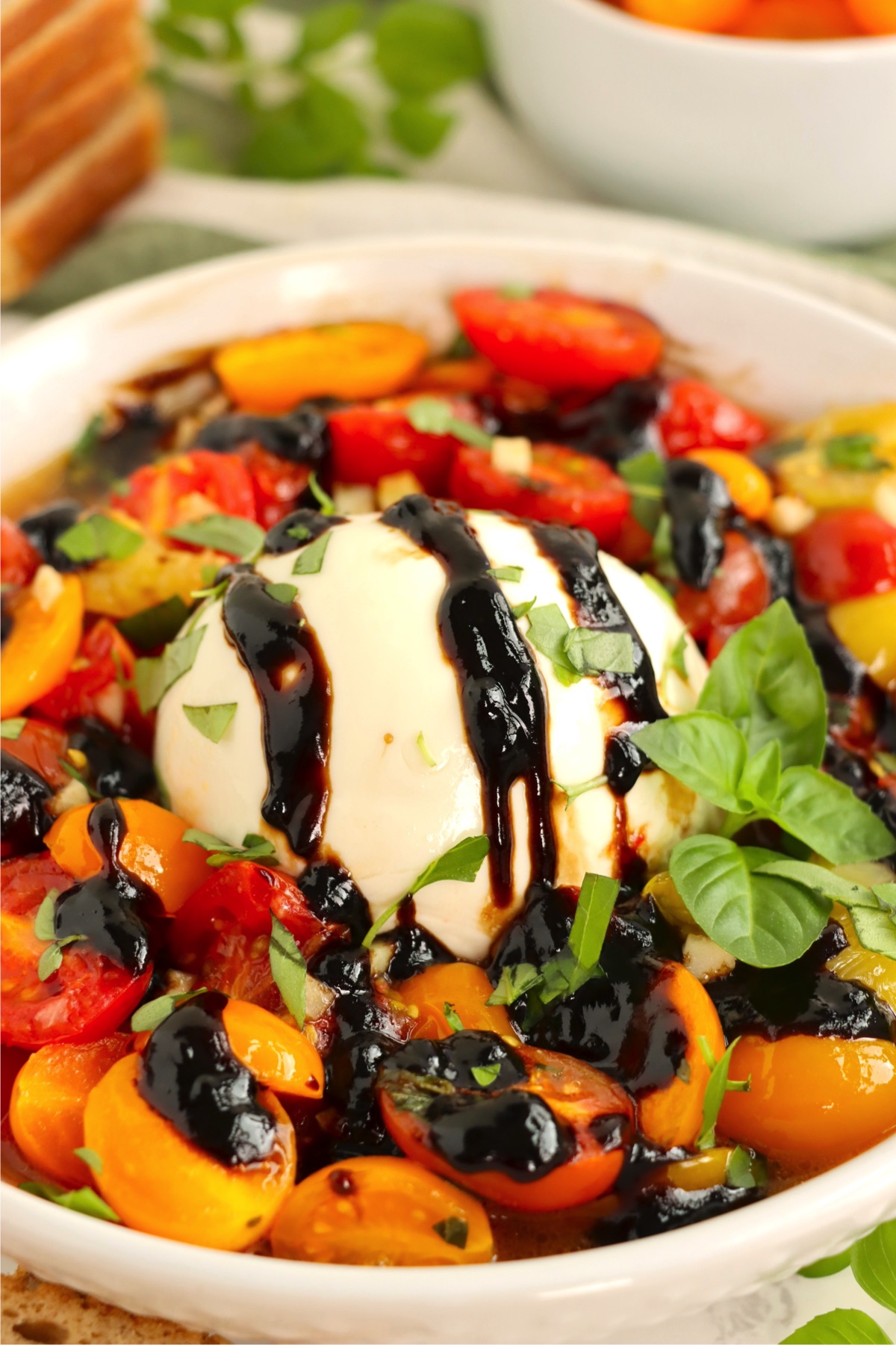 Ball of mozzarella covered with balsamic drizzle surrounded by halved cherry tomatoes.