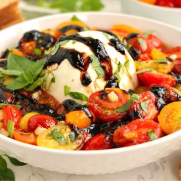 Ball of mozzarella cheese surrounded by fresh red and yellow cherry tomatoes.