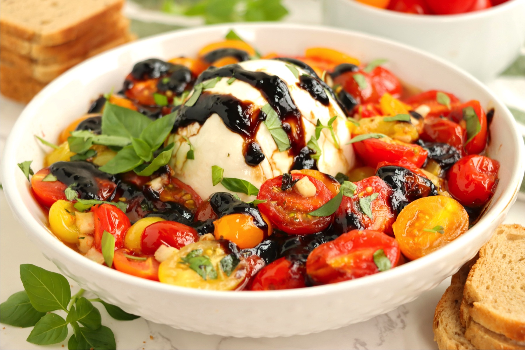 Ball of mozzarella cheese surrounded by fresh red and yellow cherry tomatoes.