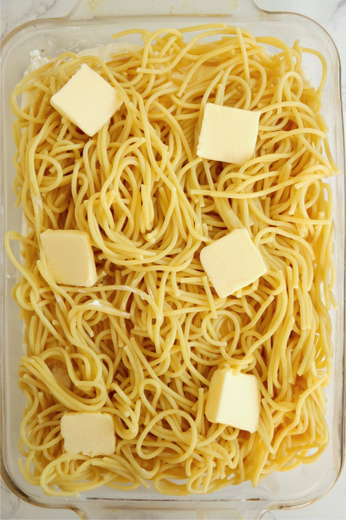 Glass baking pan filled with spaghetti and toped with slices of butter.