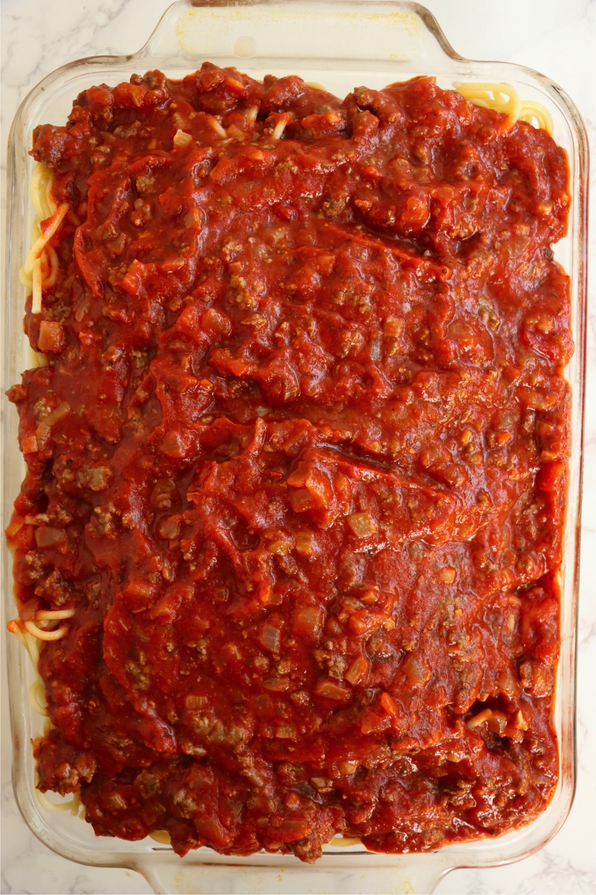 A glass pan filled with spaghetti noodles and covered in sauce.