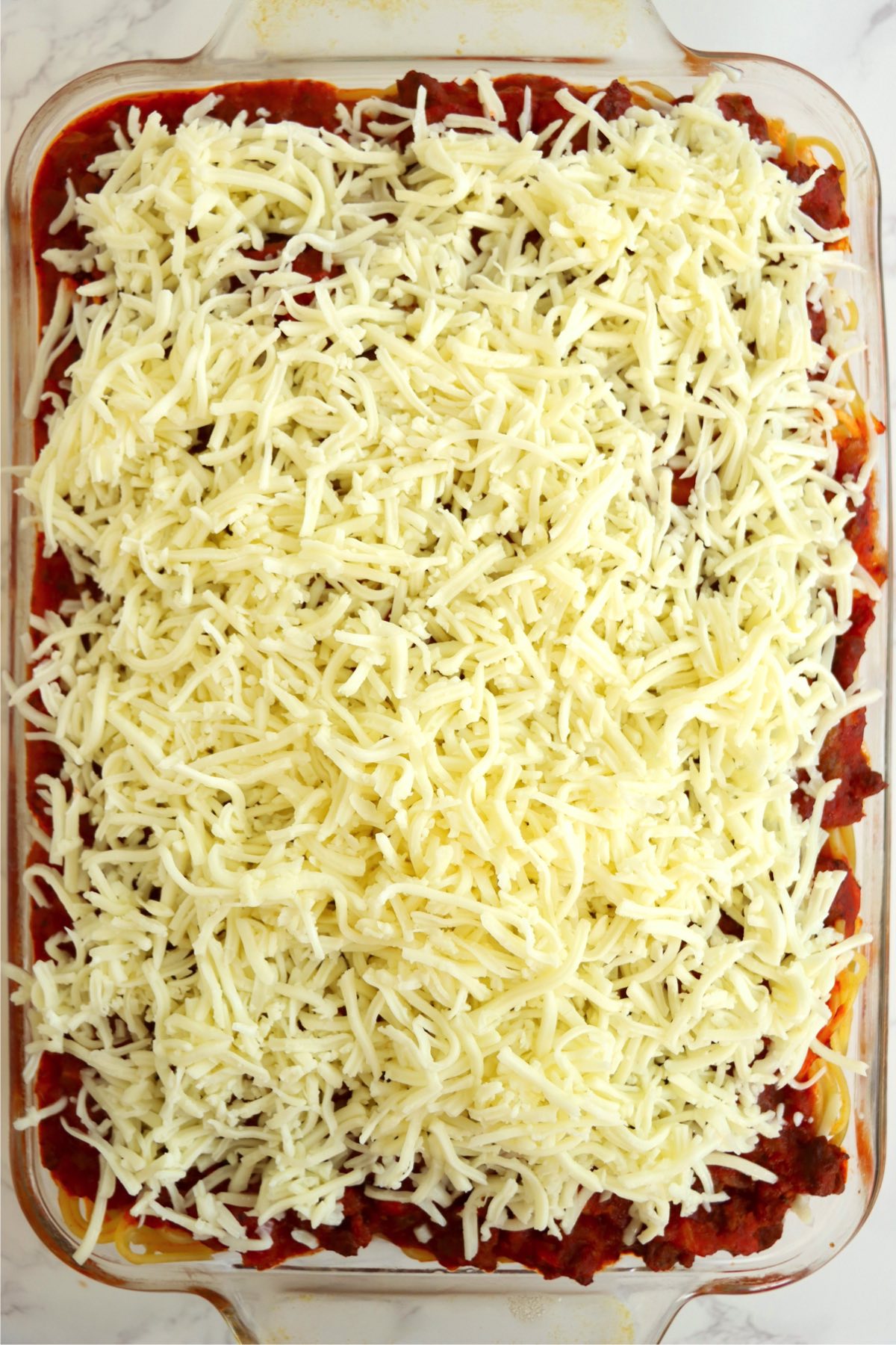 Pan of spaghetti covered in shredded mozzarella cheese.