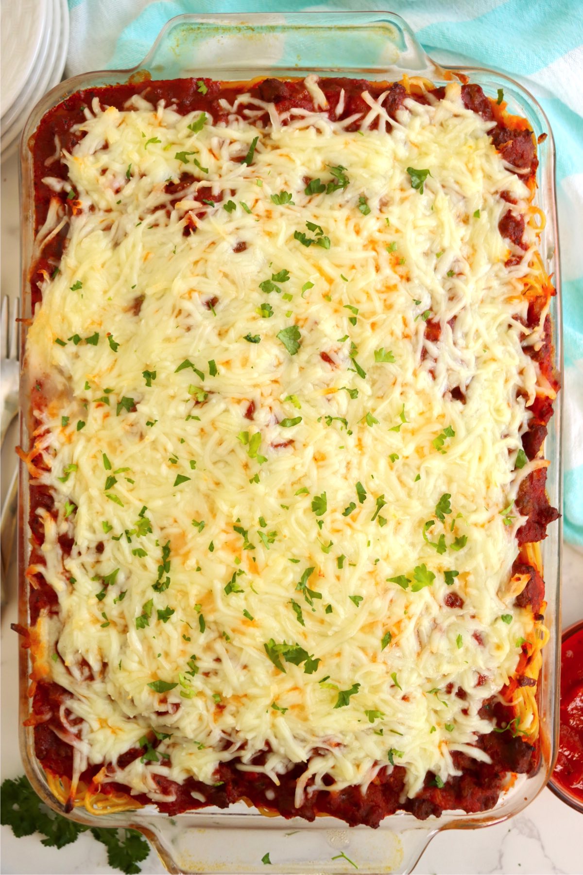 Baked pan of spaghetti covered with mozzarella cheese and garnished with parsley.