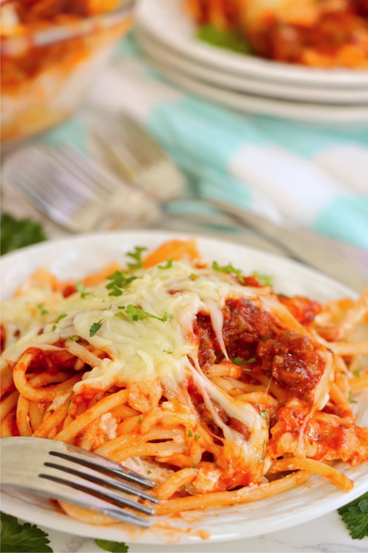 White plate filled with spaghetti noodles covered in sauce and mozzarella cheese.