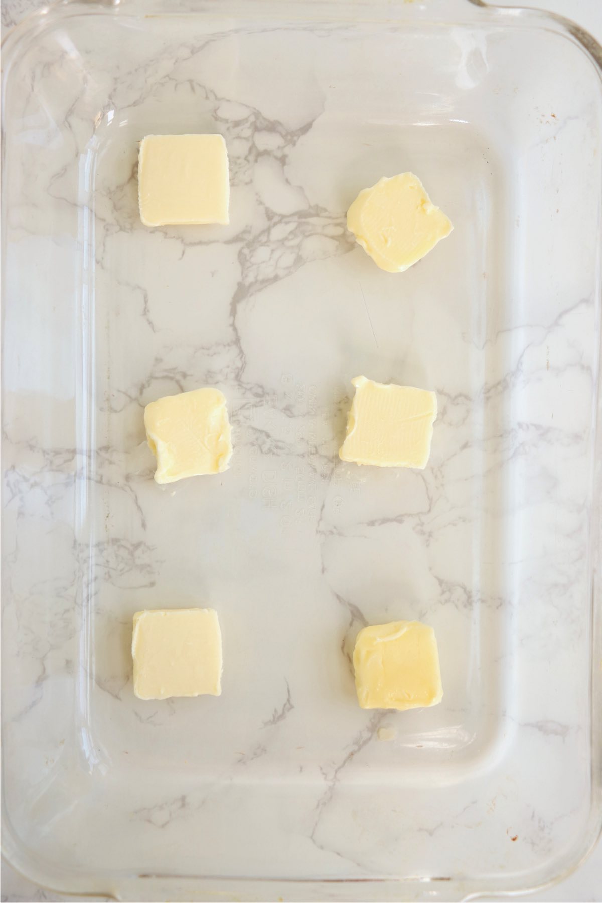 Slices of butter lining the bottom of a glass baking pan.