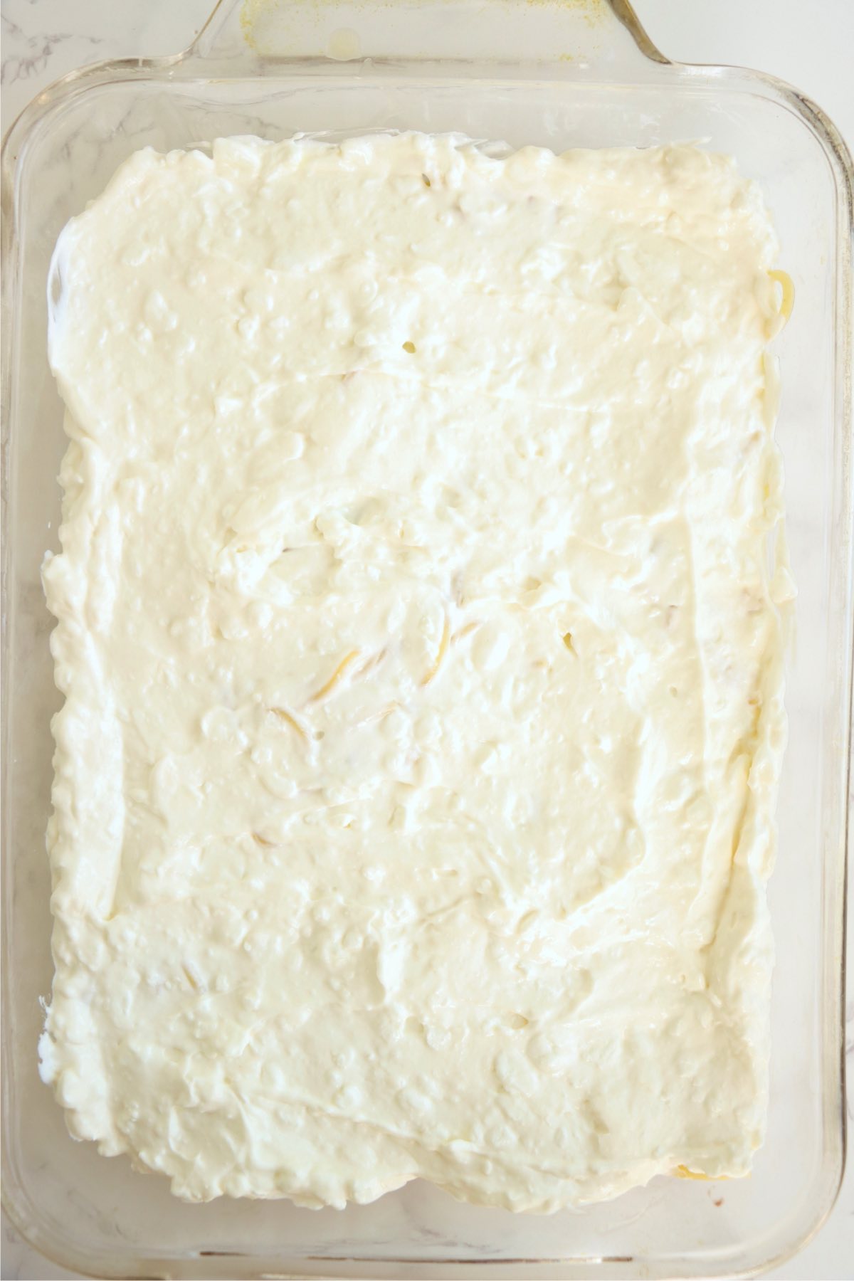 Cream cheese spread over top of spaghetti in a glass baking pan.