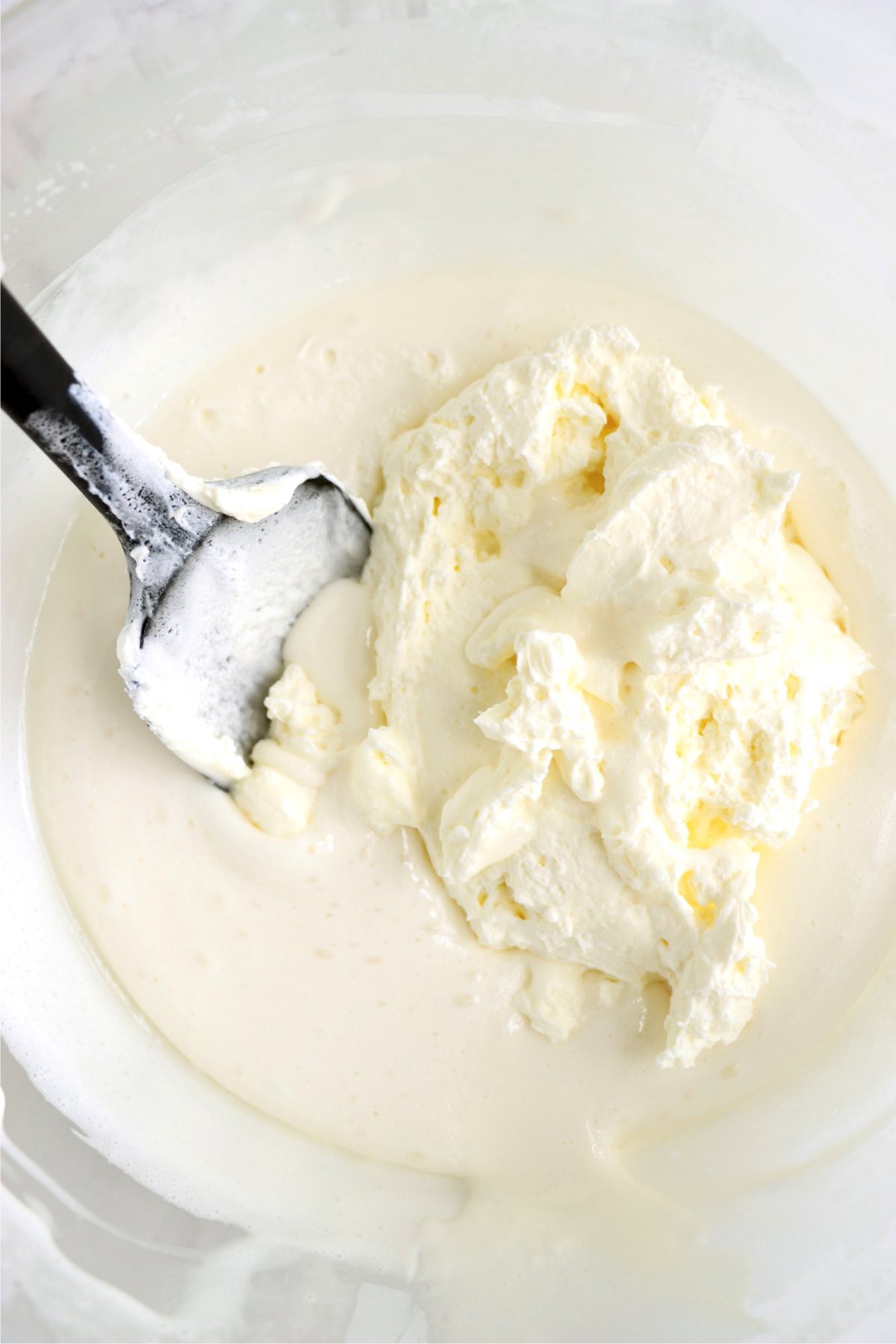 Combining heavy whipping cream and melted marshmallow in a glass bowl.