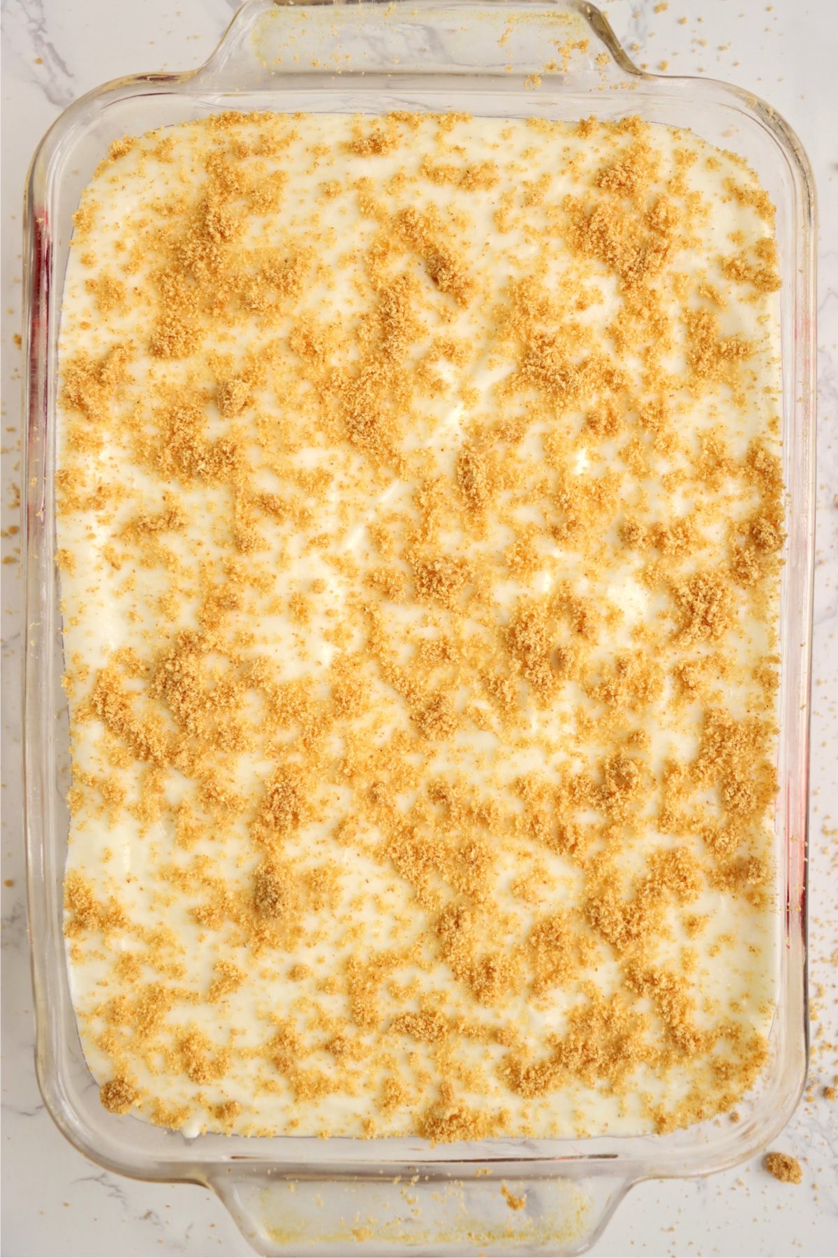 Glass baking pan filled with a crushed graham cracker garnished raspberry dessert.