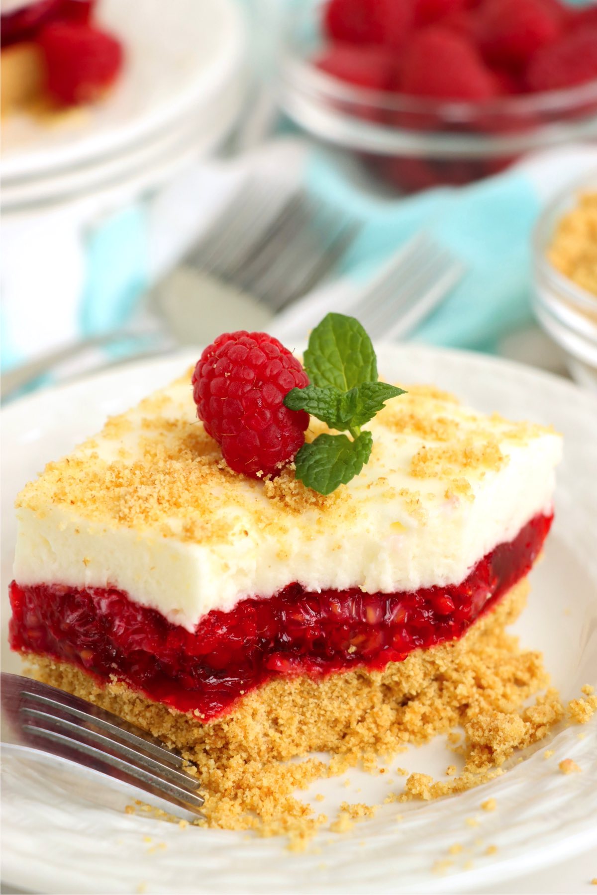 Fork digging into a piece of raspberry layered dessert with graham cracker crust.