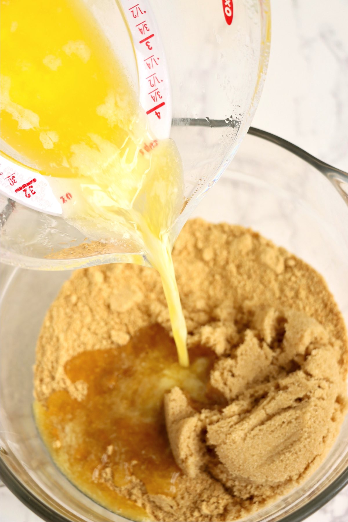 Pouring melted butter into a bowl of crushed graham crackers.