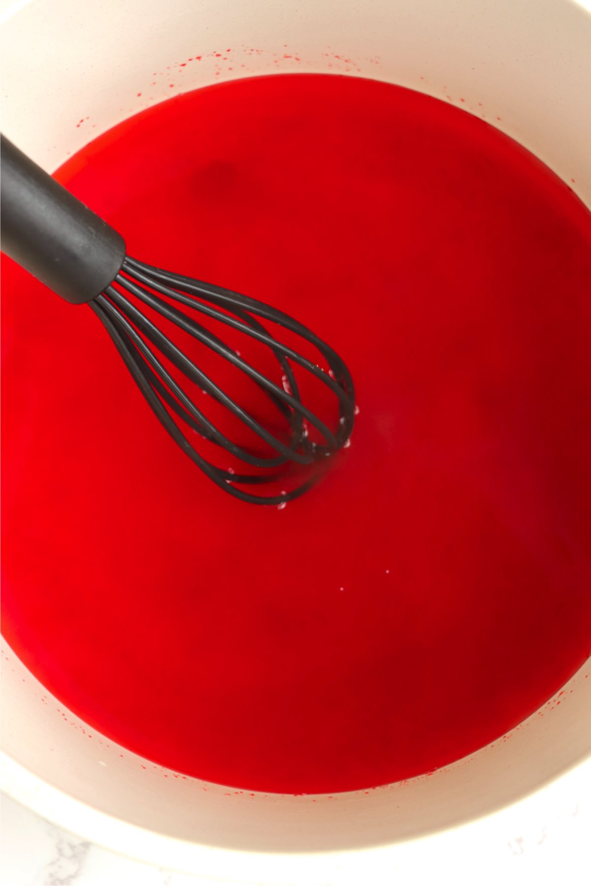 Whisking raspberry Jello in a white bowl.