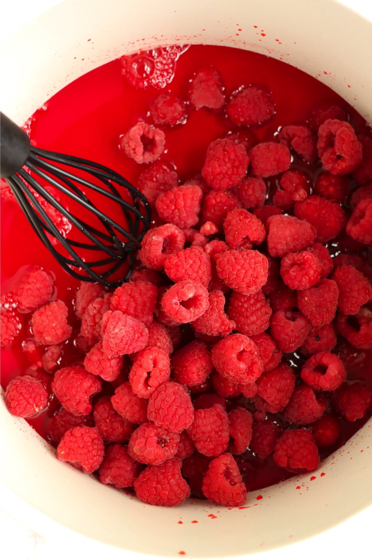 Whisking together raspberry Jello and fresh raspberries.