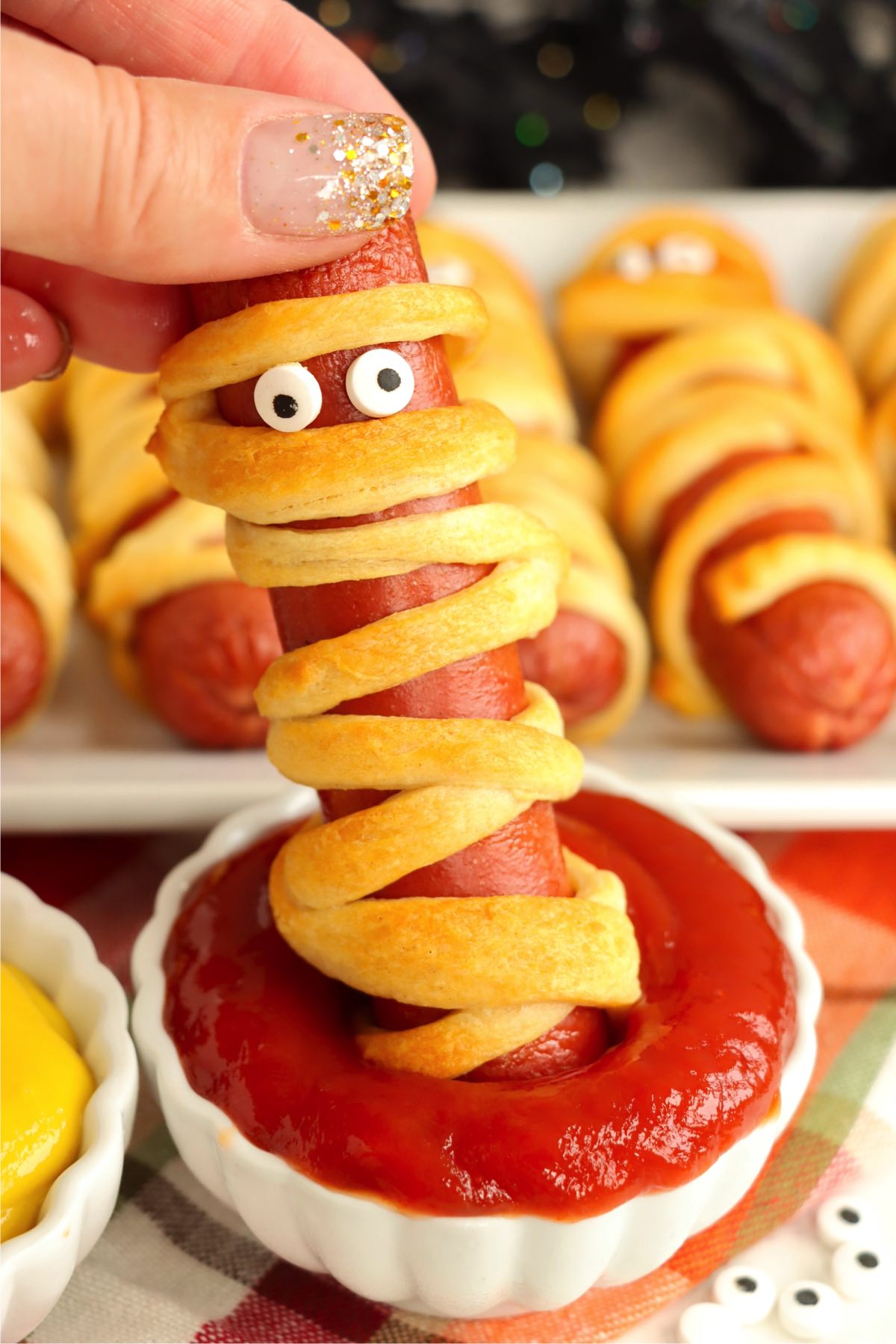 Dipping a Halloween mummy dog into a container of ketchup.