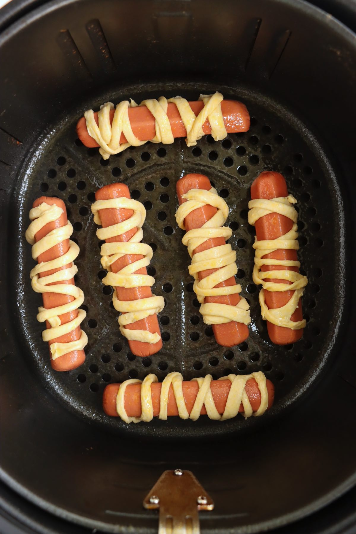 Crescent roll wrapped hotdogs laid in an air fryer basket.