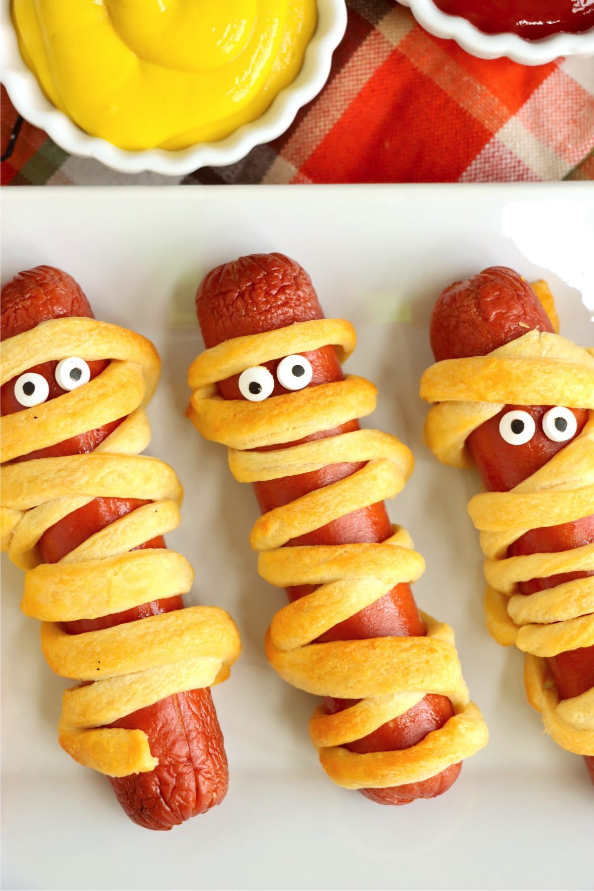 Mummy dogs with candy eyes laid out on a white platter.