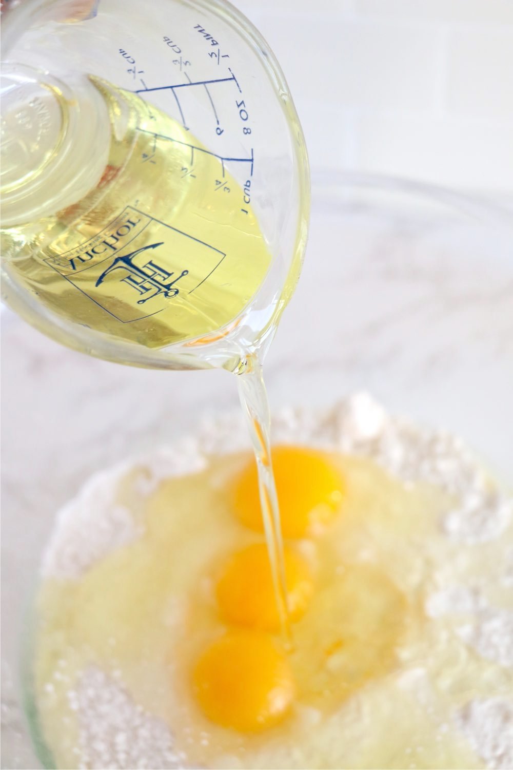 Pouring oil from a measuring cup into a bowl of eggs and flour.