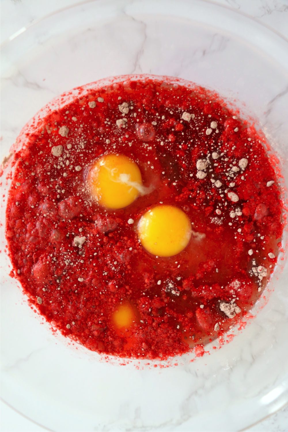 Bowl of red cake mix with two eggs yokes.