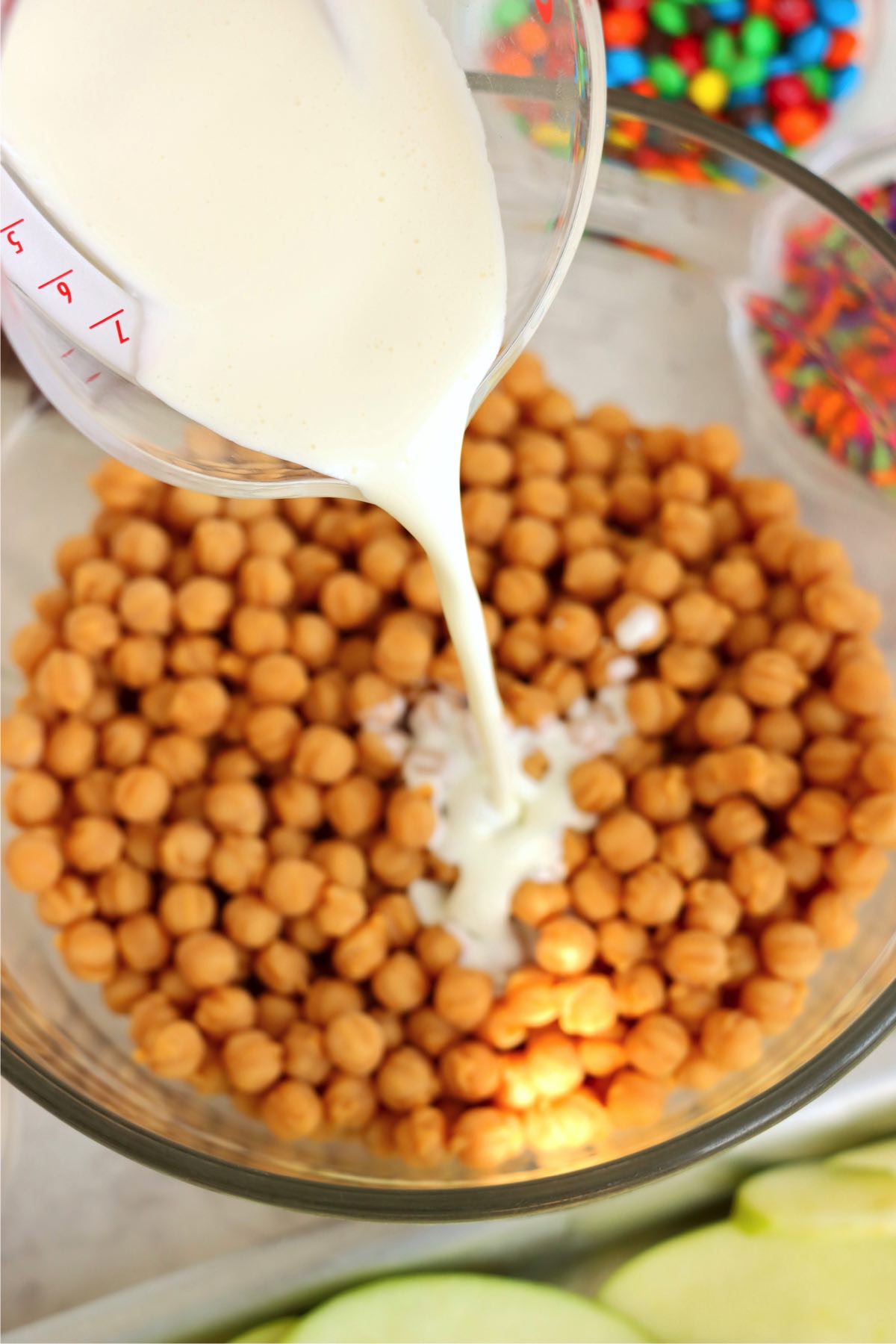 Pouring milk from a measuring cup into a bowl of caramel bits.