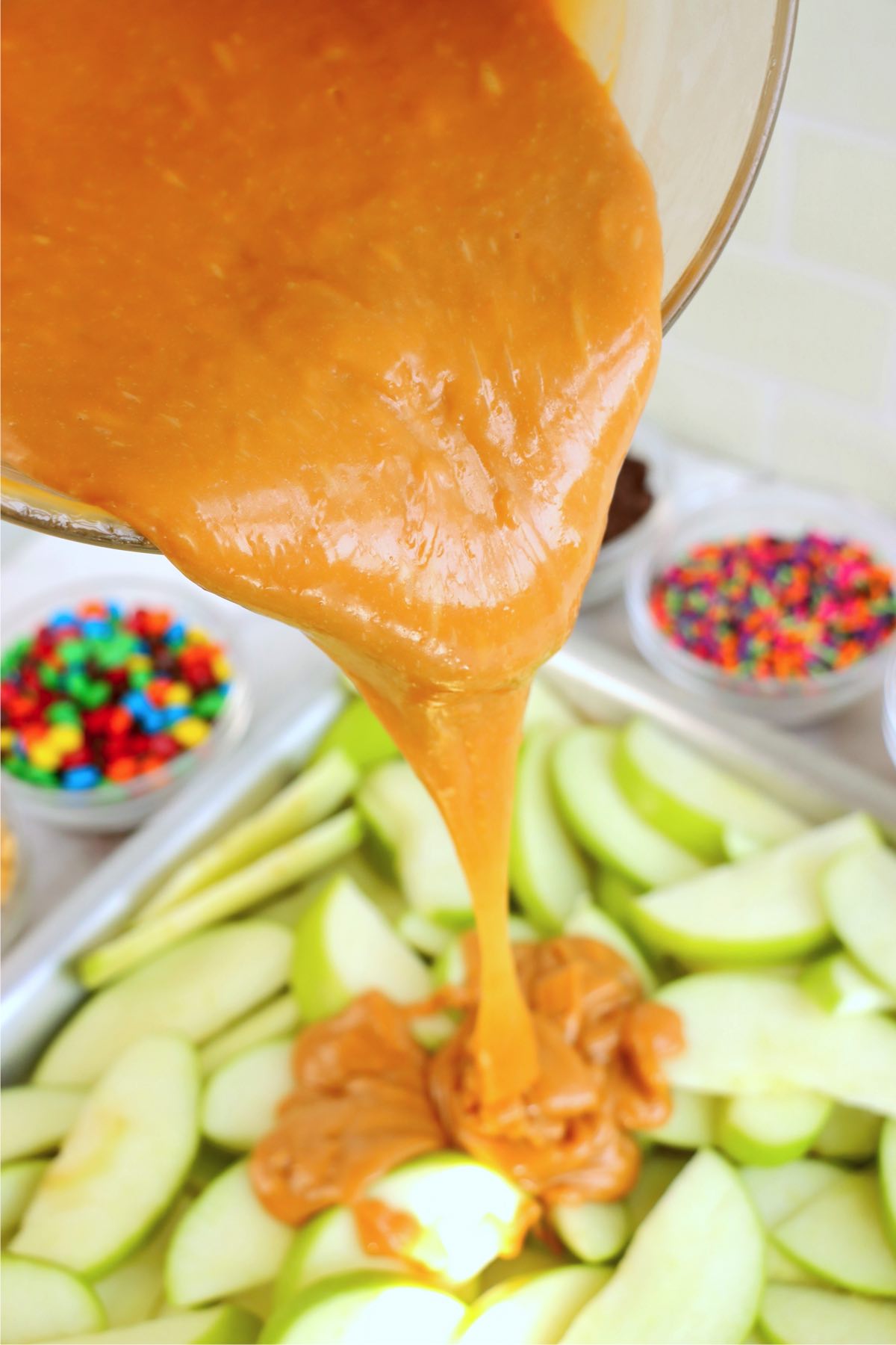 Pouring melted caramel over the top of sliced green apples.