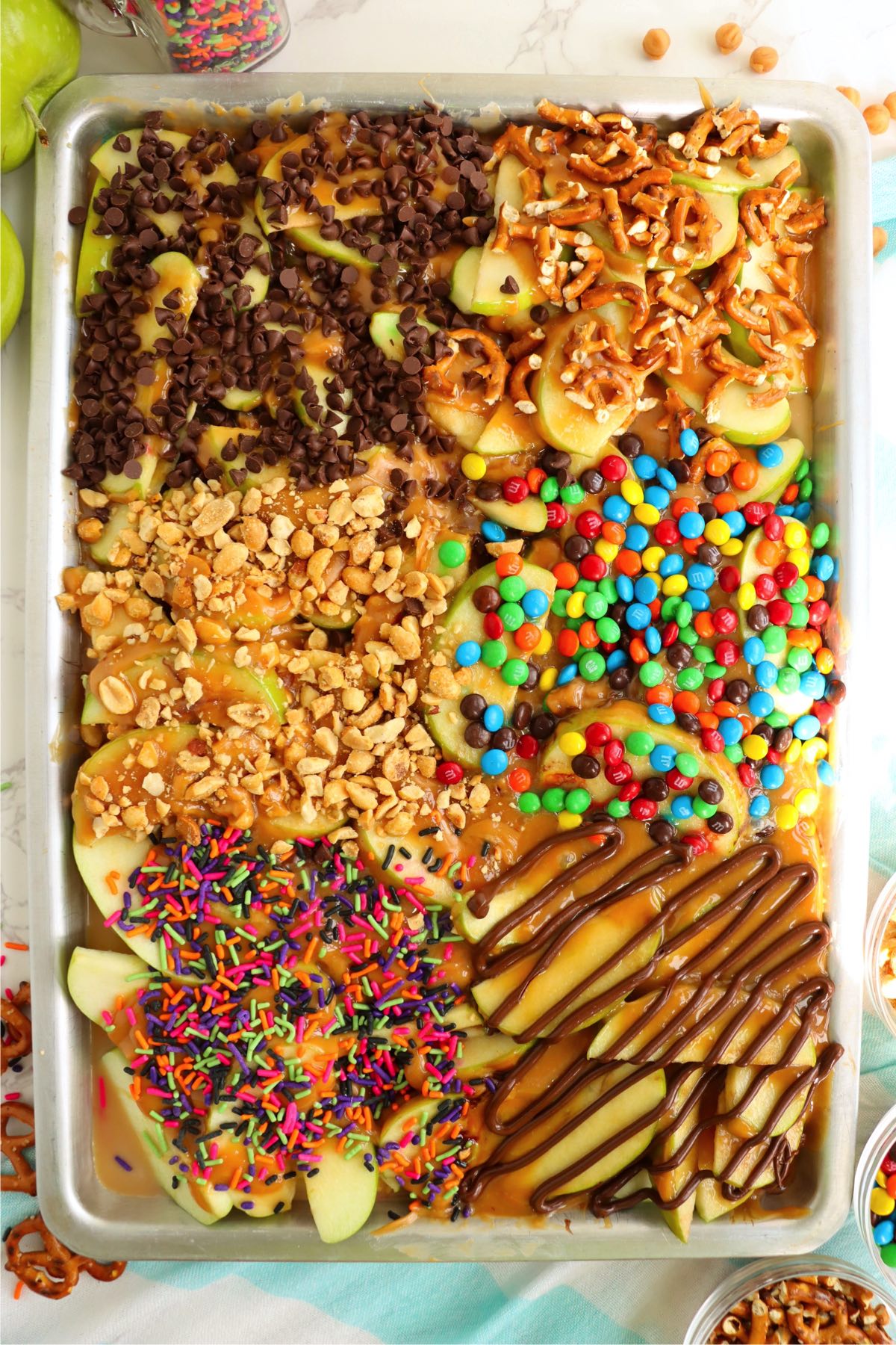 Sheet pan filled with sliced caramel apples and nut and candy toppings.