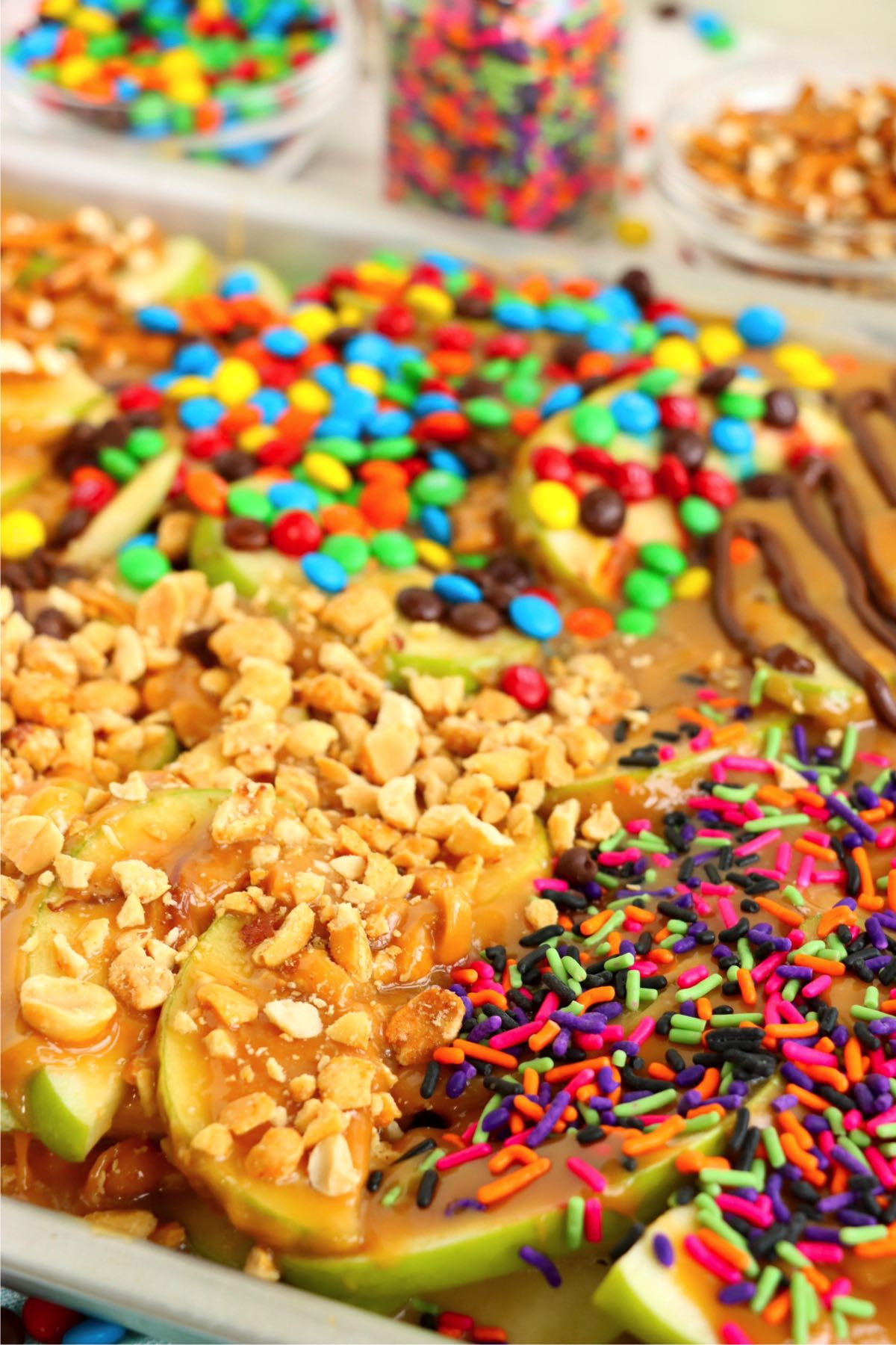 Sliced apples on a pan covered with caramel and nut and candy toppings.