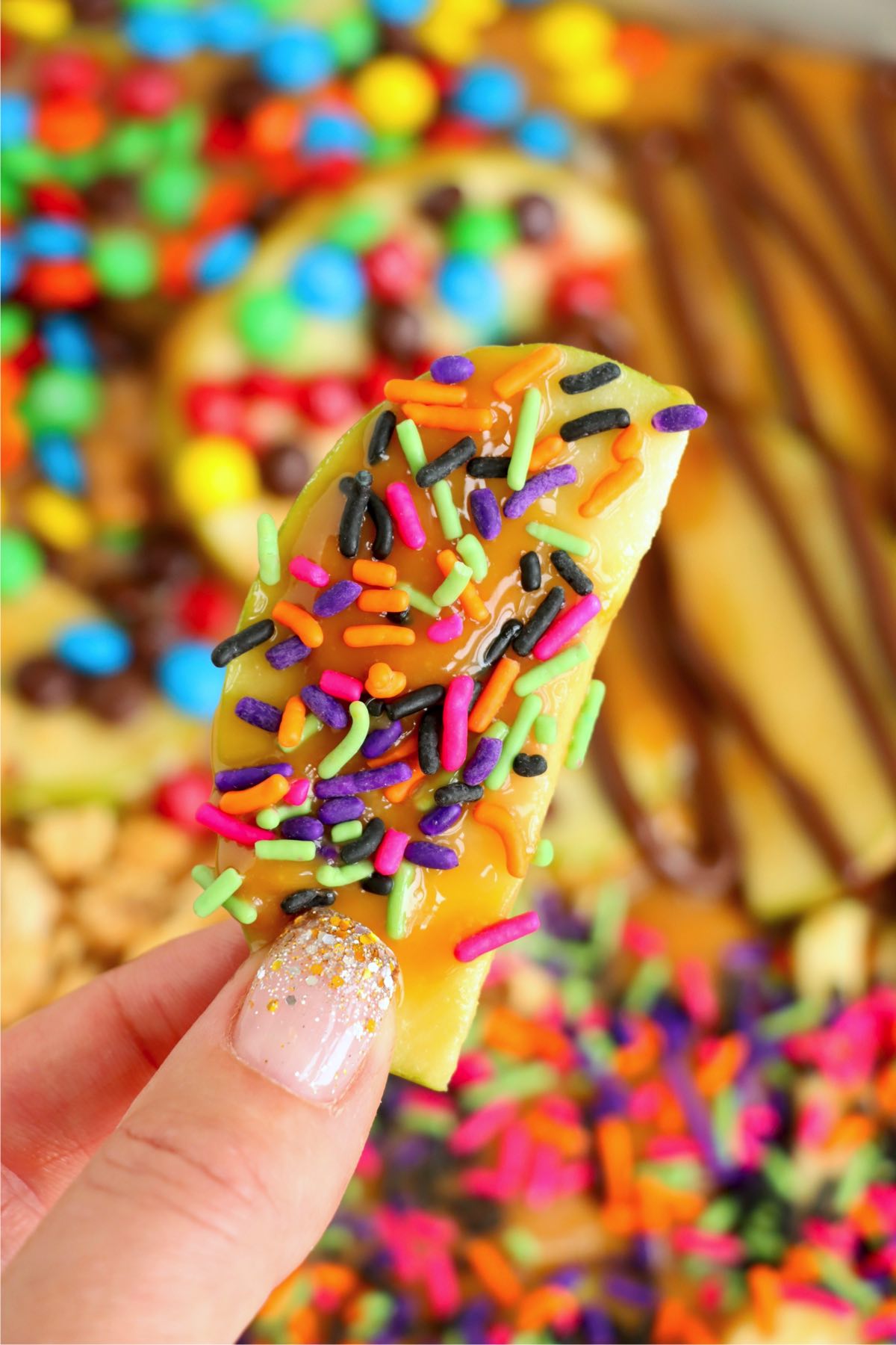 Hand holding an apple slice covered in caramel and sprinkles.