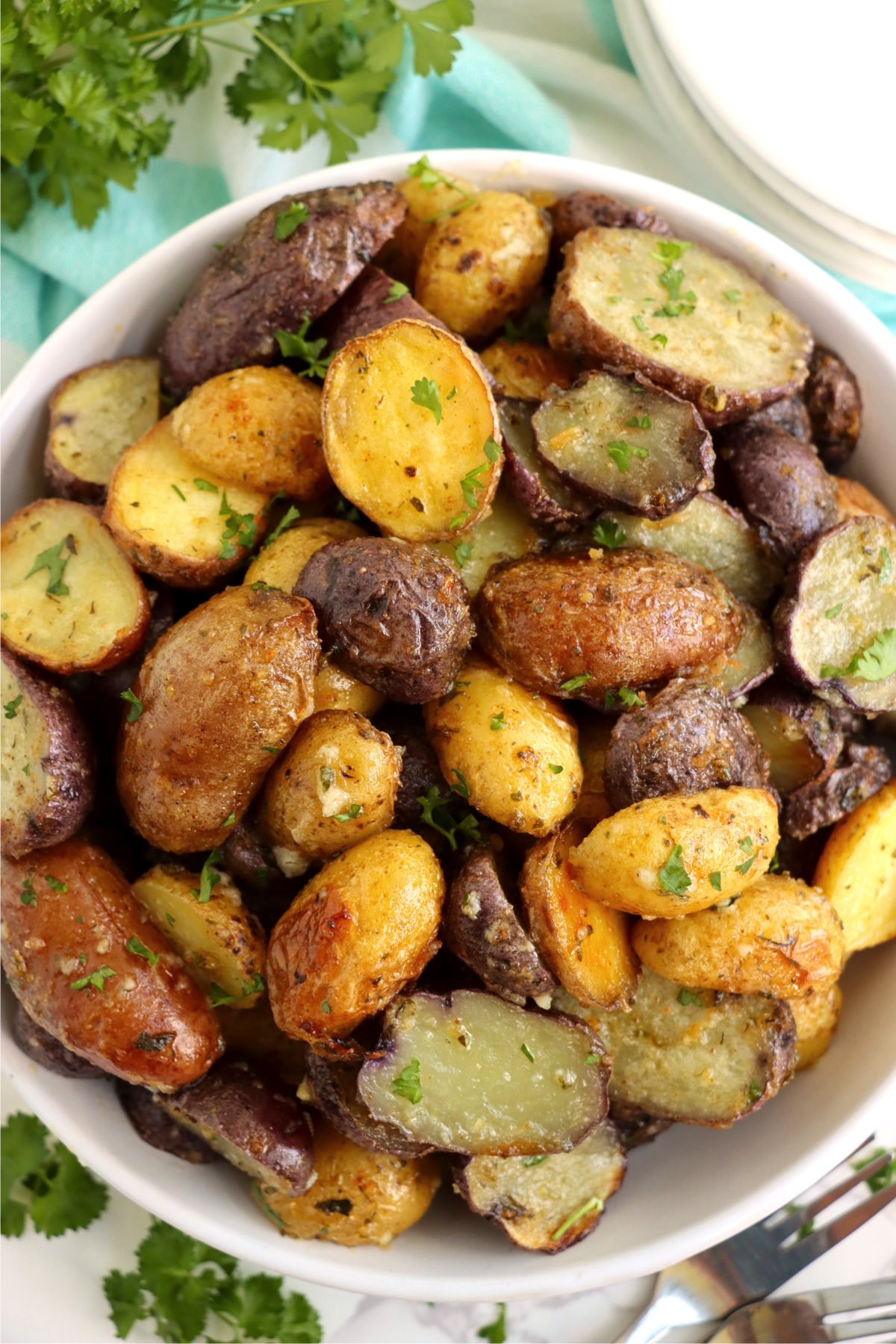 Bowl of roasted fingerling potatoes surrounded by parsley.